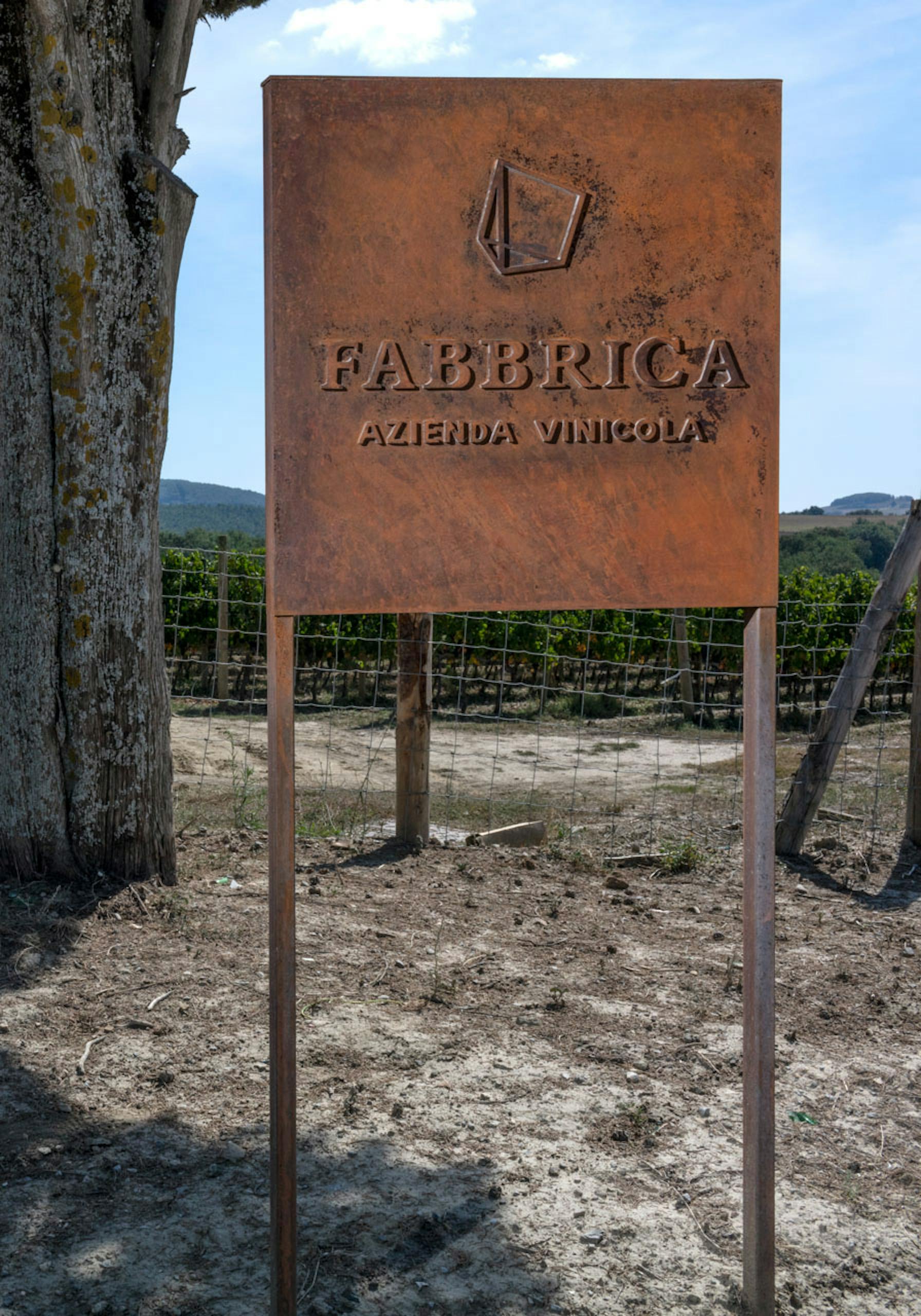 Entrance of Fabbrica with a tractor on the strada bianca, cypresses alongside and the sign of the winery